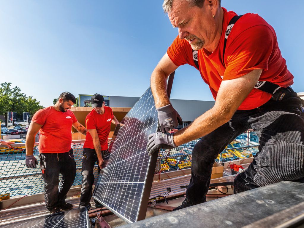 3 Männer bauen eine Solarzelle auf das Dach eines Hauses