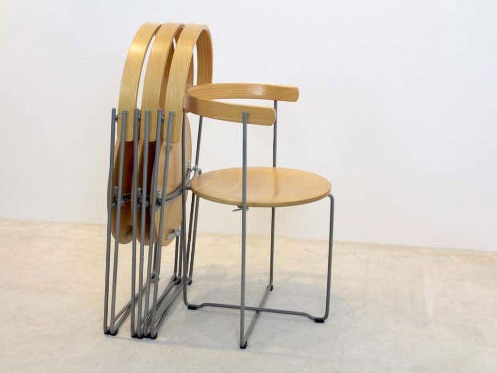 Zwei zusammengeklappte Holzstühle lehnen an einem ausgeklappter Klappstuhl aus Holz