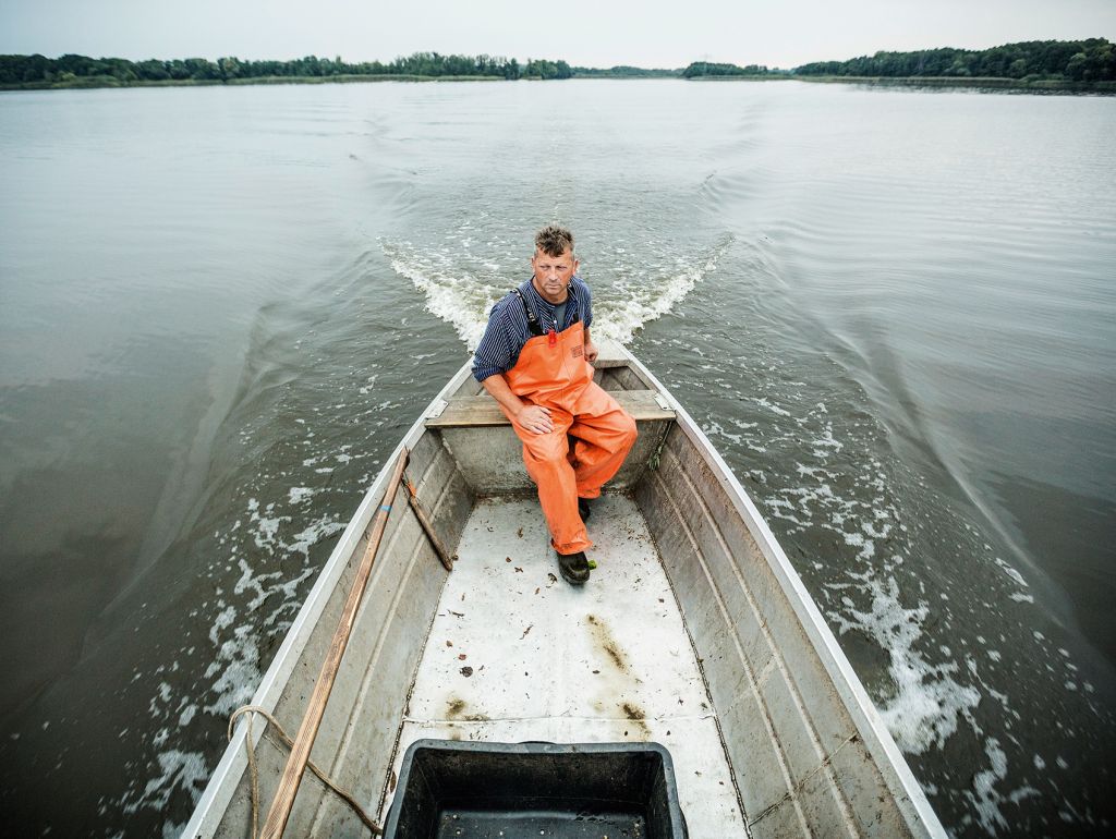 Ein Mann steuert ein Holzboot über einen See