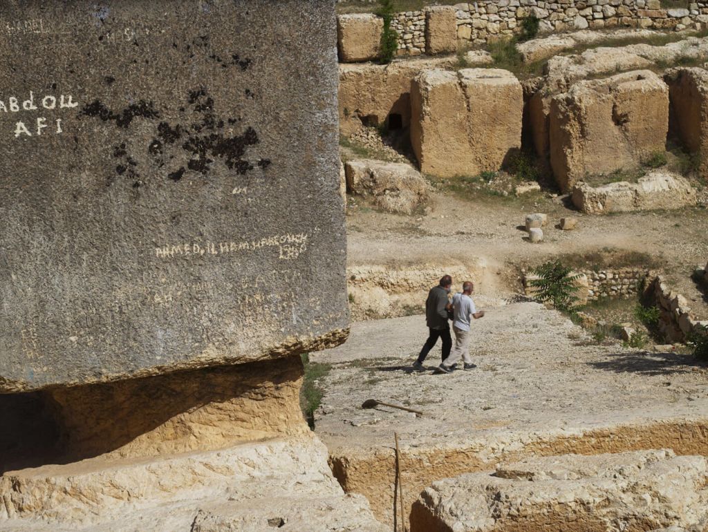 Ein Steinbruch mit großem schwarzen Stein im linken Vordergrund  und zwei personen im hintergrund mittig