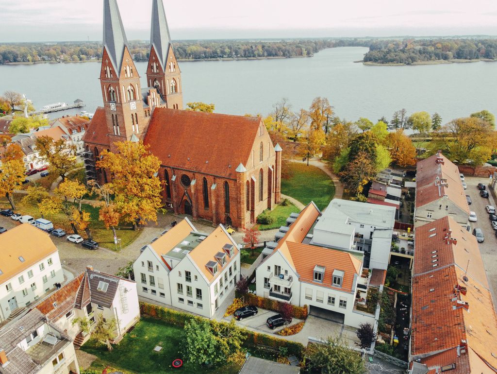 Luftbildaufnahme einer Kirche mit 2 Türmen direkt am See