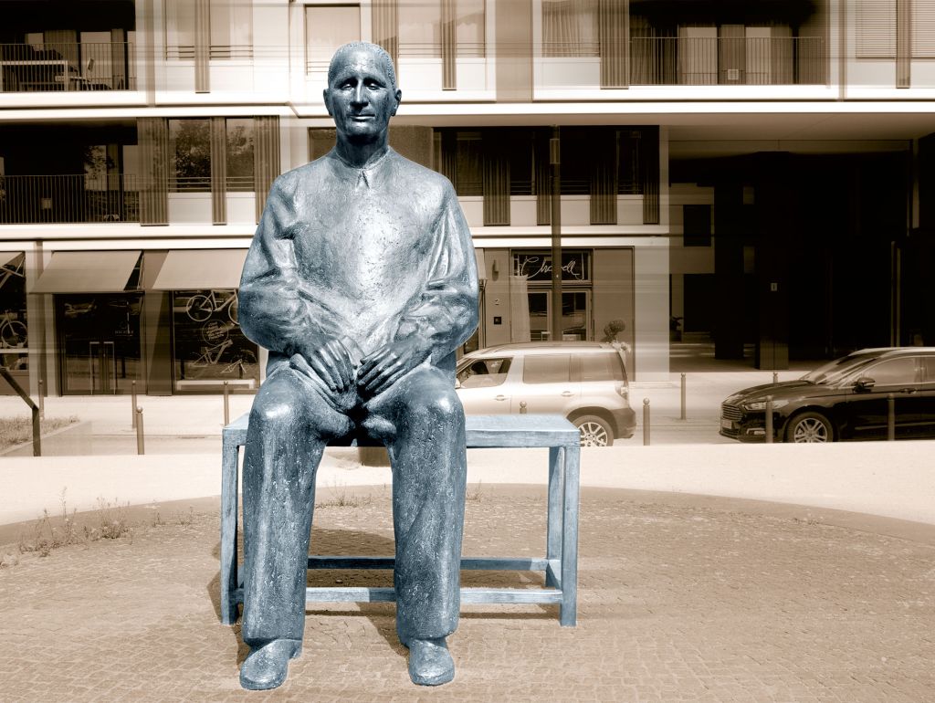 Eine Statue von Bertold Brecht sitzend auf einer Bank vor einem Neubau