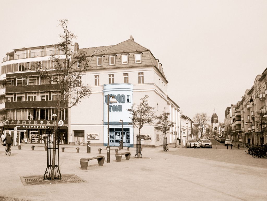 Der Antonplatz: Bäume, der Eingamg zu einem Kino, eine Apotheke und im Hintergrund eine Kirche 