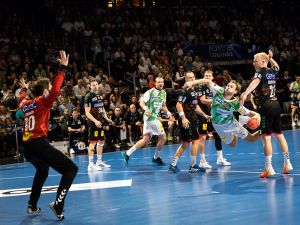 Eine Gruppe von Männern, die auf einem Platz Handball spielen, dribbeln, schießen und gegeneinander antreten