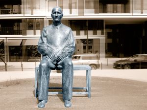Eine Statue von Berthold Brecht sitzend auf einer Bank vor einem Neubau